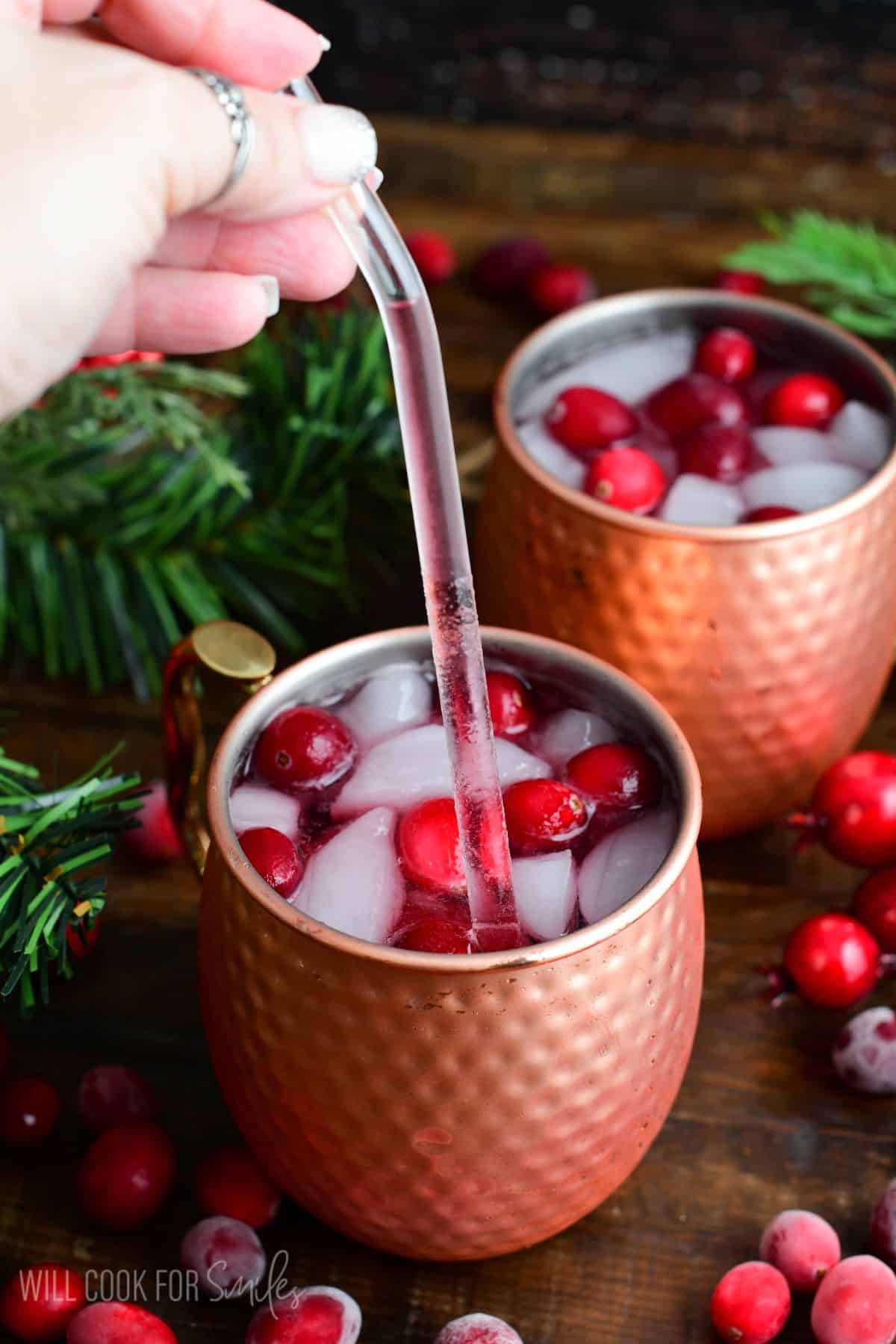 two copper mugs with cranberry Moscow mule in them with a straw with some of the mule in it.