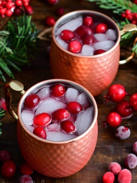 Two cranberry Moscow Mules with fresh cranberries and ice in a copper mug.