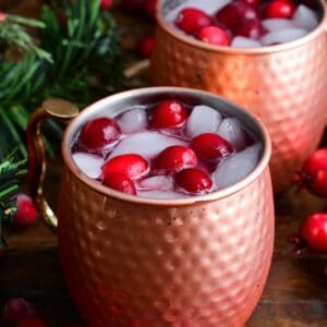 Two copper mugs with cranberry Moscow Mule with fresh cranberries and ice.
