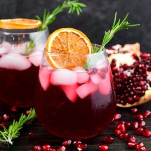 gin cocktail perfect for winter time in a glass with orange and rosemary and pomegranates around.