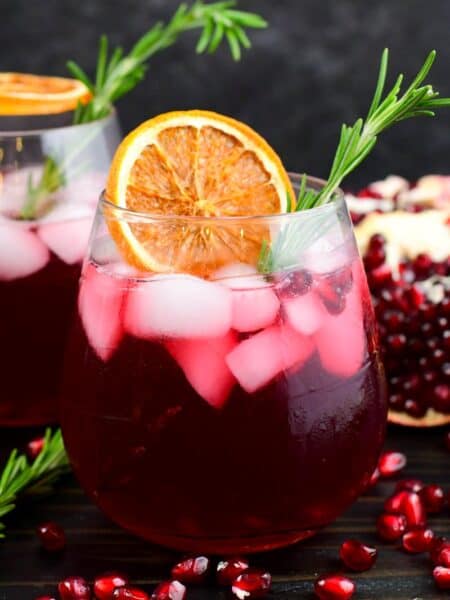 gin cocktail perfect for winter time in a glass with orange and rosemary and pomegranates around.