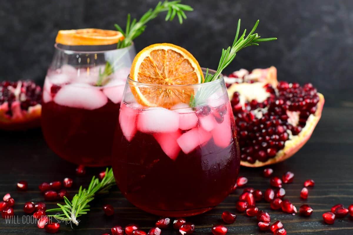 gin cocktail perfect for winter time in a glass with orange and rosemary and pomegranates around.