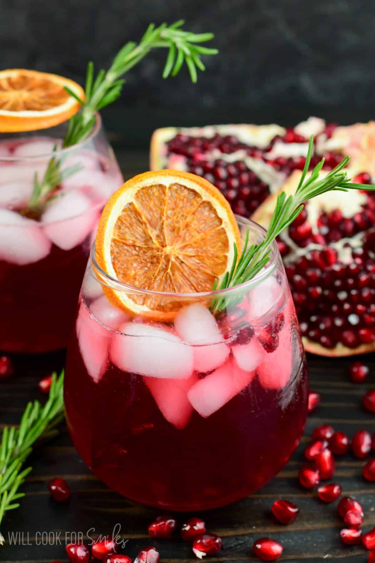 Beautifully deep red pomegranate gin cocktail in a glass garnished with orange and rosemary.