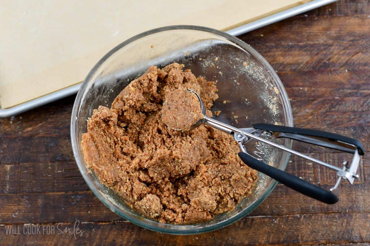 Rumchata rum ball dough in a glass bowl with a small cookie scoop.