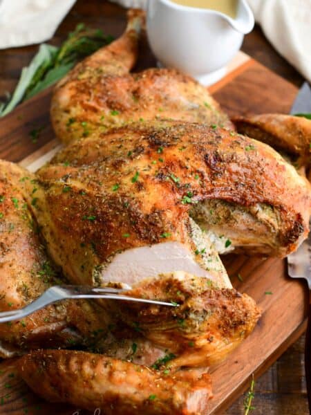 Cutting into the juicy breast of golden roasted spatchcock turkey on a wood cutting board.