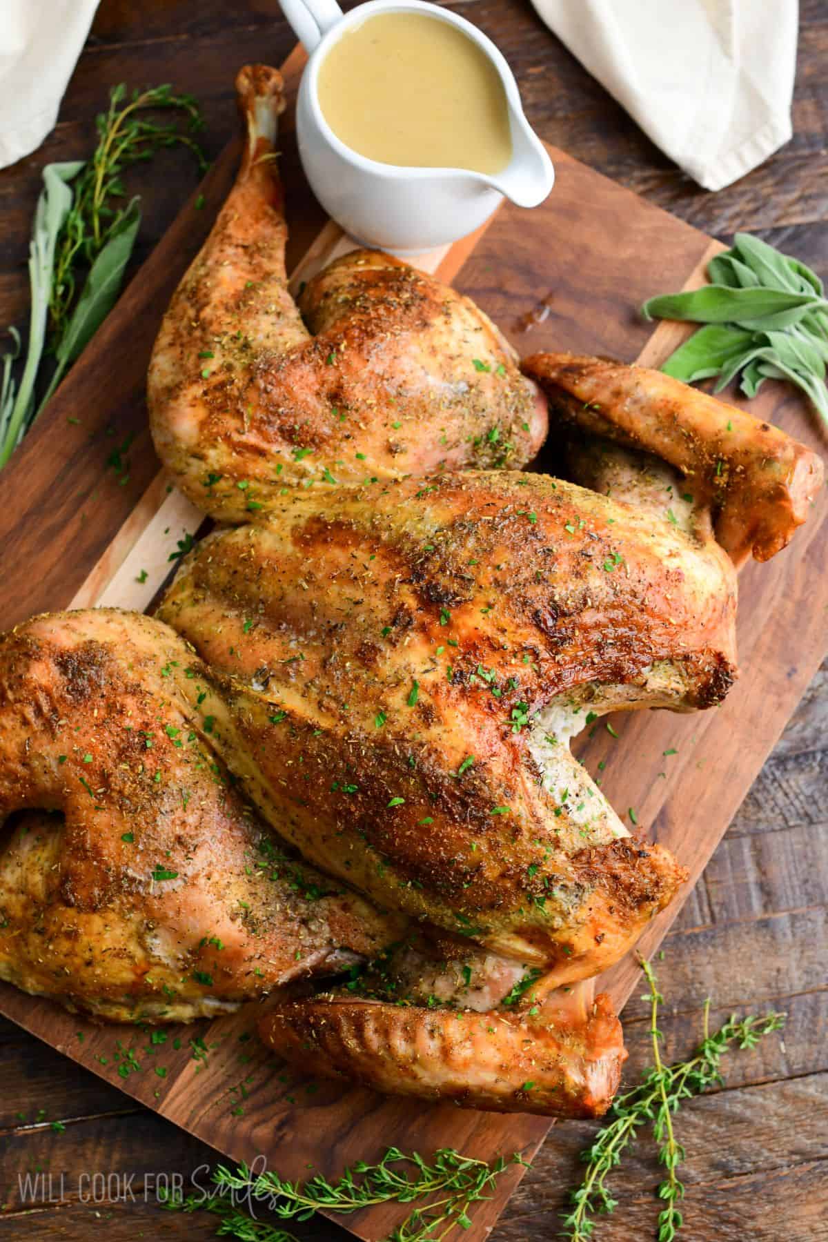 seasoned, golden brown roasted Spatchcock Turkey with turkey gravy on the side on a wood cutting board.