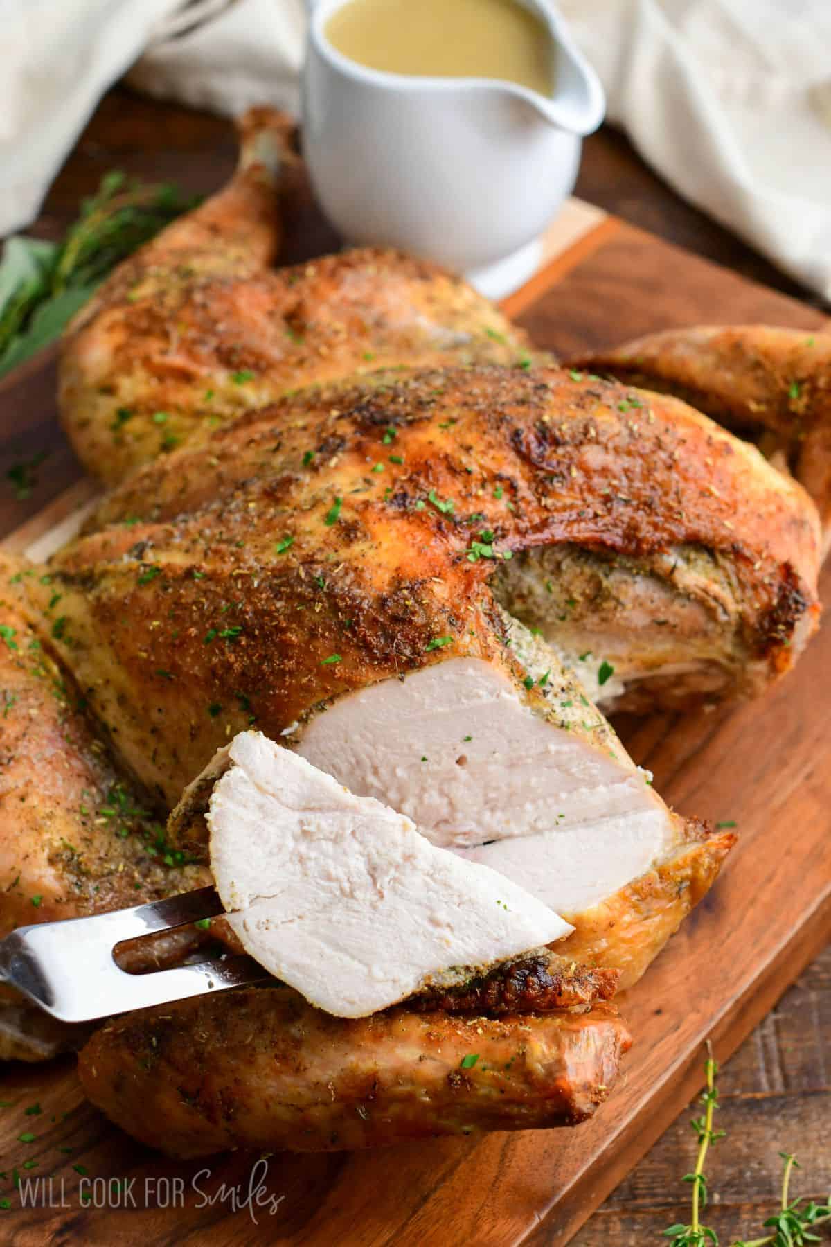 Taking a juicy slice out of the breast of spatchcock turkey with a serving fork to show juicy breast meat.