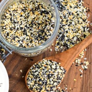 a jar full of everything seasoning next to a spoon and some spread on the cutting board.