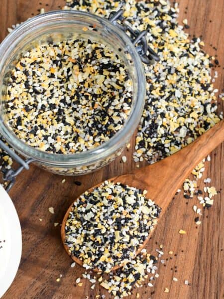 a jar full of everything seasoning next to a spoon and some spread on the cutting board.
