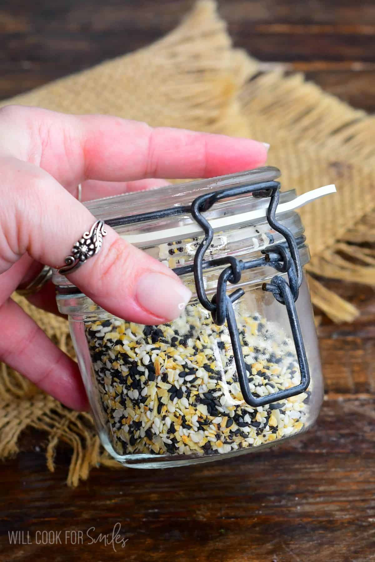 shaking a glass jar full of everything bagel seasoning to mix.