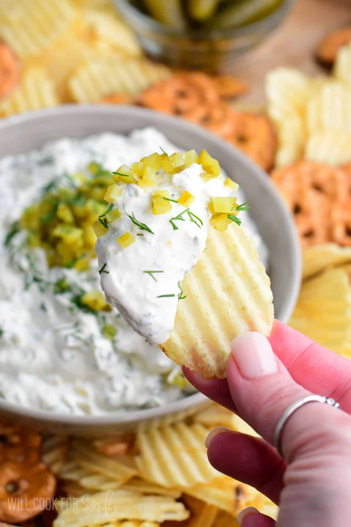 Pickle dip scooped with a chip and the bowl of dip in the background.