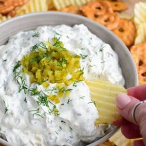 Using a potato chip to scoop some pickle dip out of the bowl.