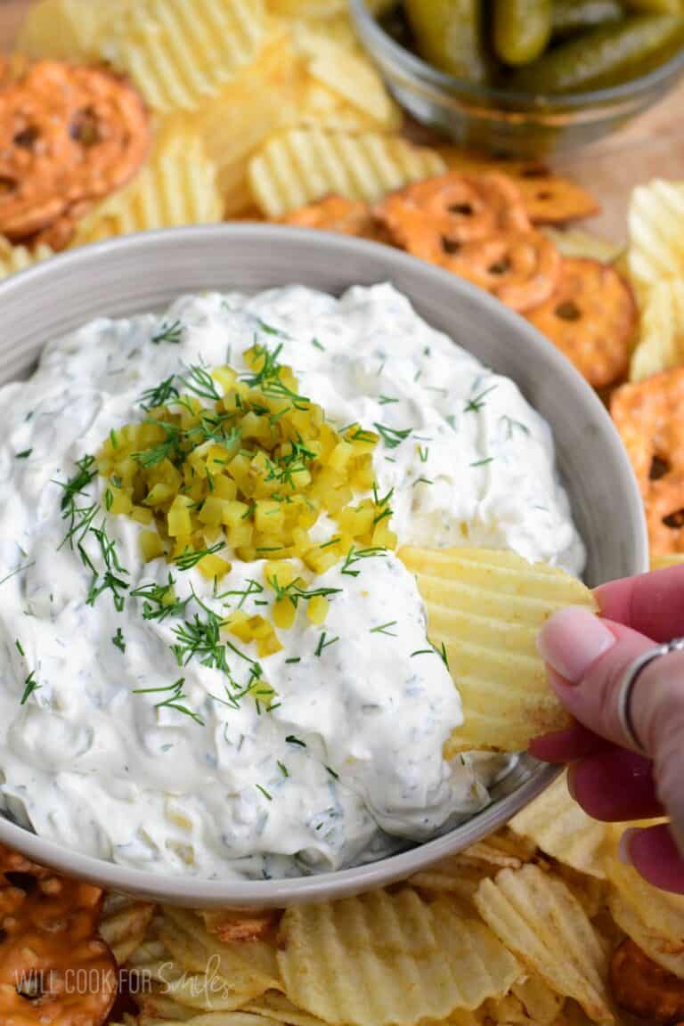 Using a potato chip to scoop some pickle dip out of the bowl.
