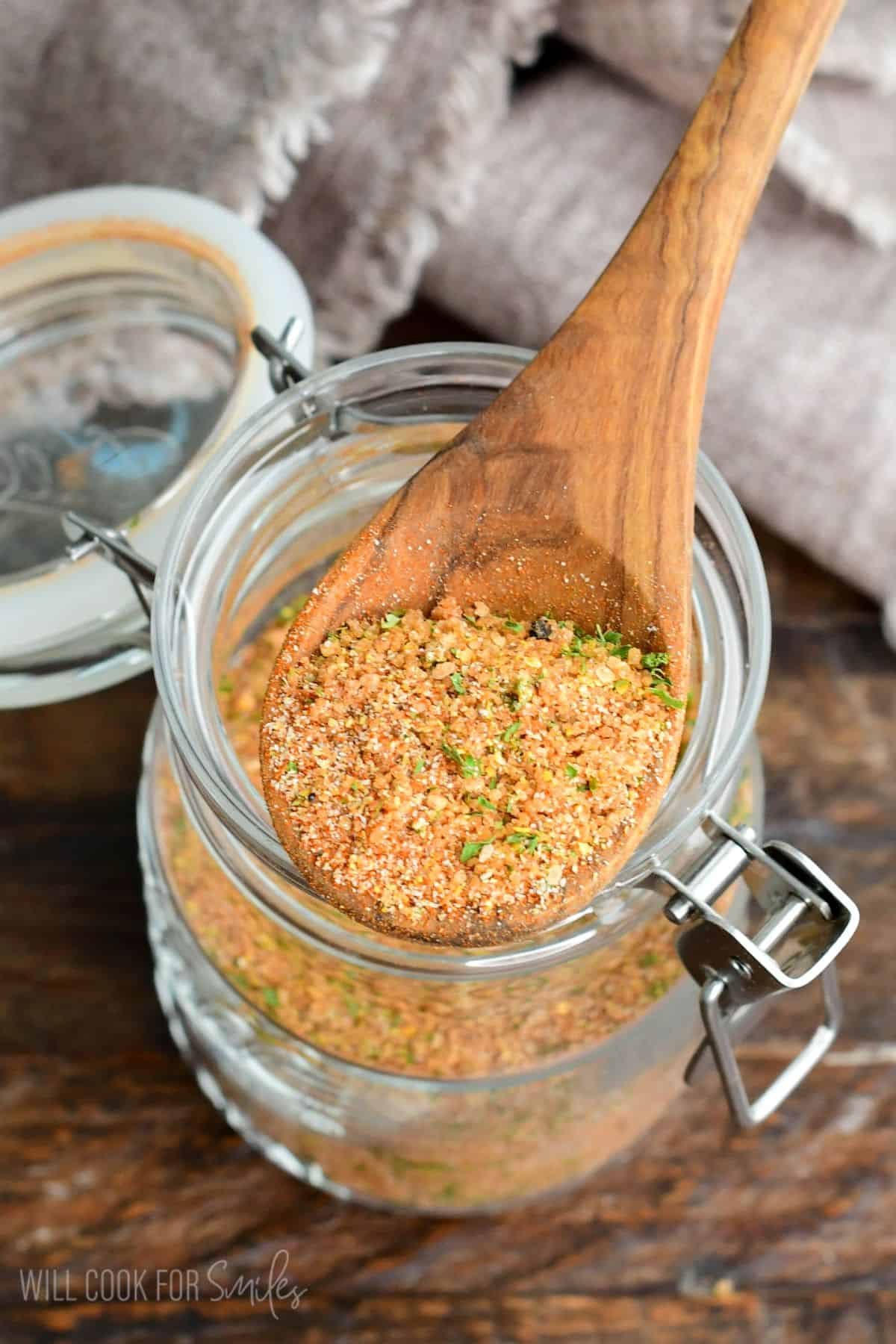 a wooden spoon with pork rub seasoning on top of a glass jar.