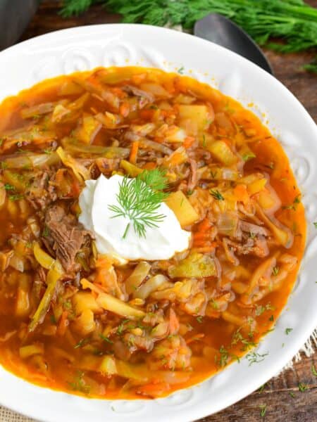 Russian beef and cabbage soup (shchi) in a white bowl with sour cream and dill and a spoon next to it.
