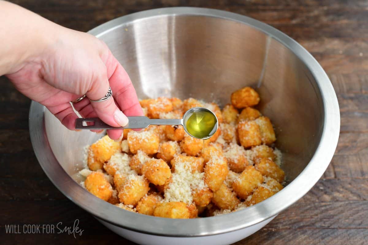 Adding the truffle oil to the bowl of cooked tater tots and parmesan cheese.
