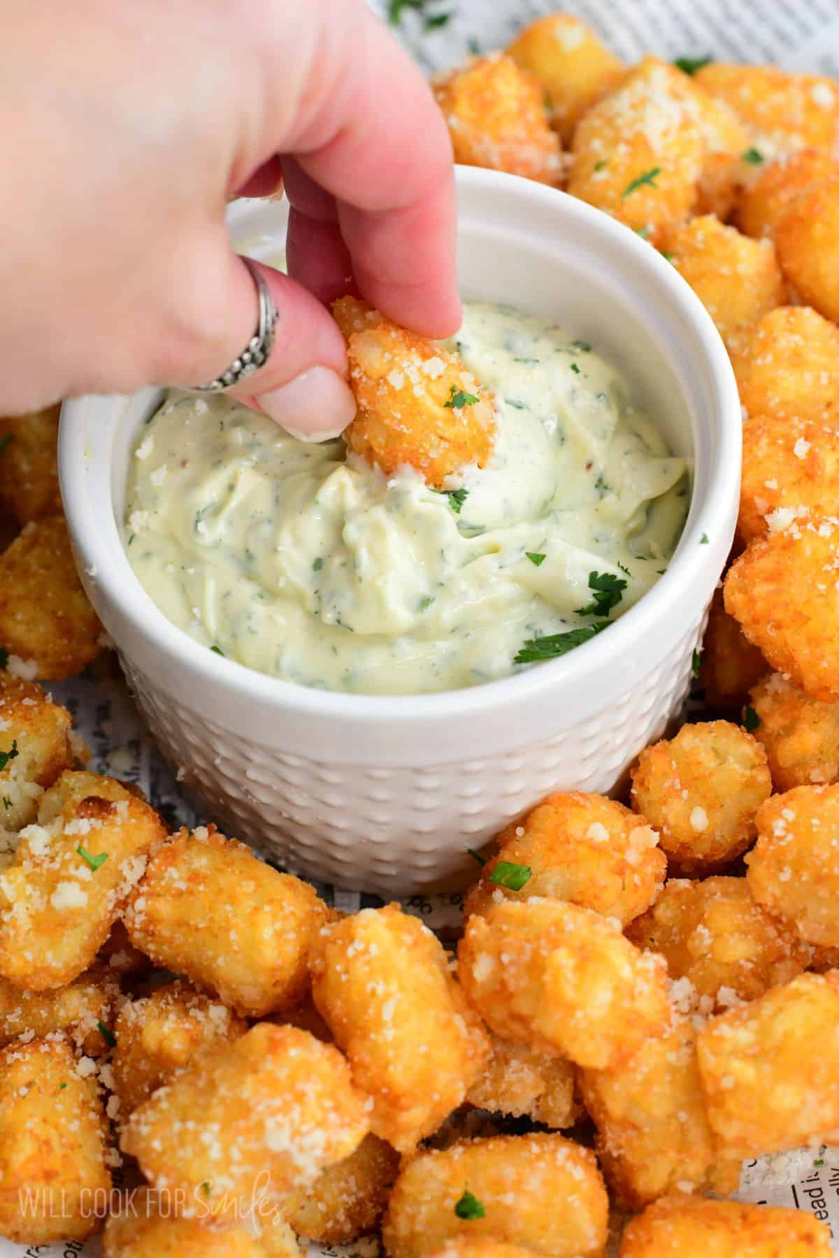 Dipping a truffle tater tot into the bowl of garlic herb aioli on the tray.