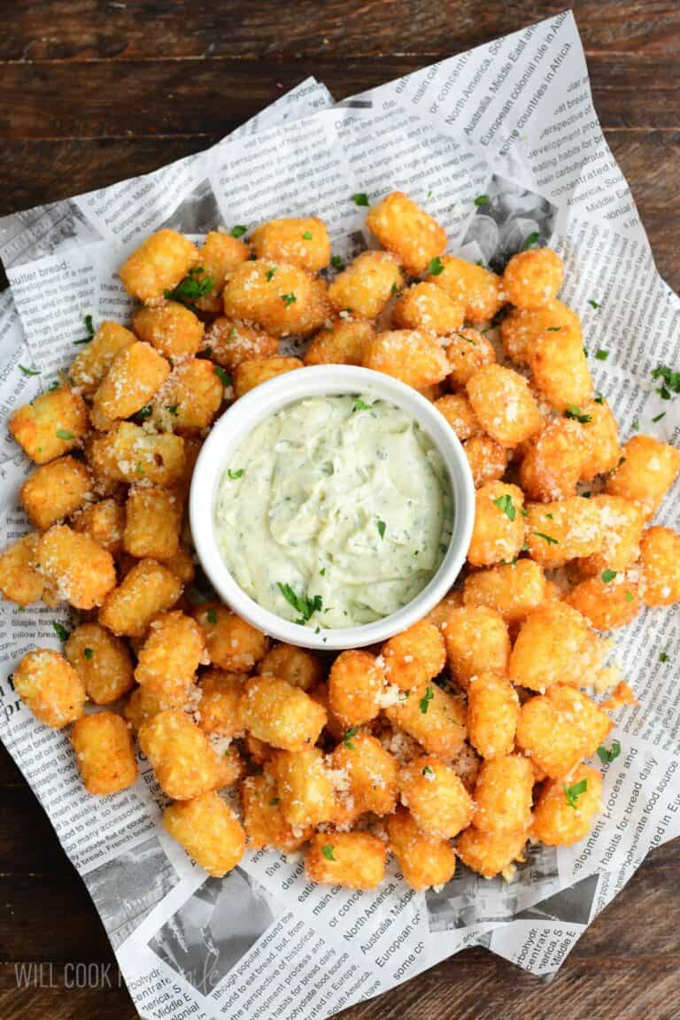 Truffle tater tots on a lined tray with a garlic herb aioli in a bowl in the middle on a wood surface.