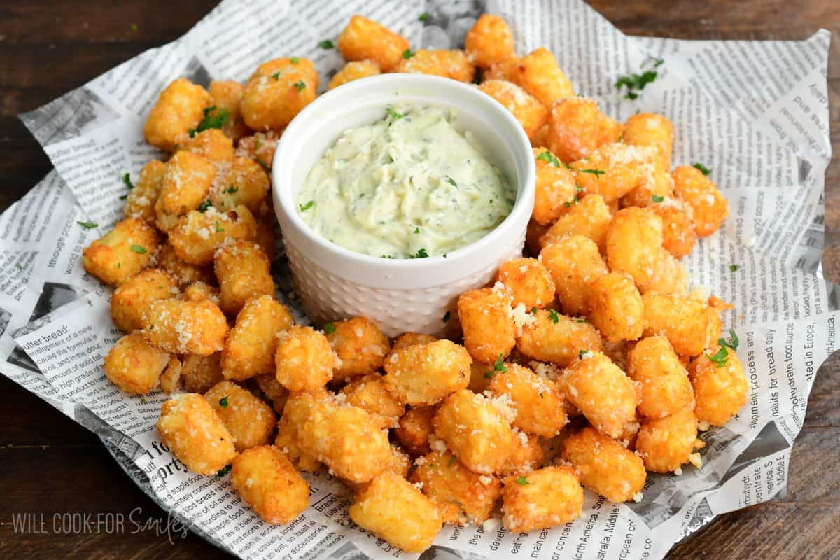 Truffle tater tots on a tray with a garlic herb aioli in a bowl in the middle.
