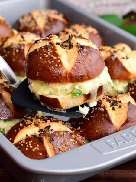 A baked jalapeño ranch chicken slider on a pretzel bun being lifted from the pan, showing melted cheese and creamy chicken filling.
