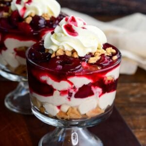 No-bake cherry cheesecake parfait layered with creamy cheesecake filling, crushed cookies, cherry topping, and whipped cream in a glass dessert cup.