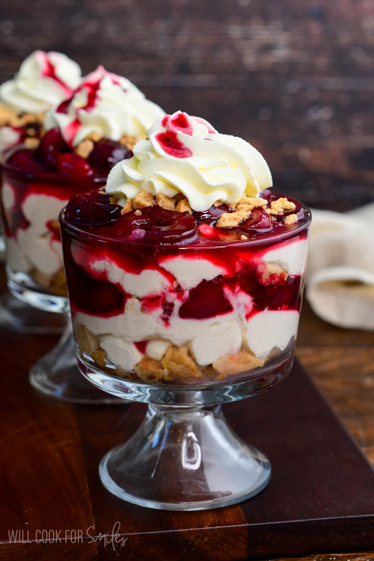 No-bake cherry cheesecake parfait layered with creamy cheesecake filling, crushed cookies, cherry sauce, and topped with whipped cream in a glass dessert cup.