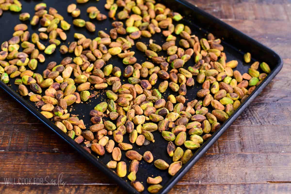 Shelled pistachios spread across a black baking sheet, lightly toasted and ready to use in pistachio tiramisu.