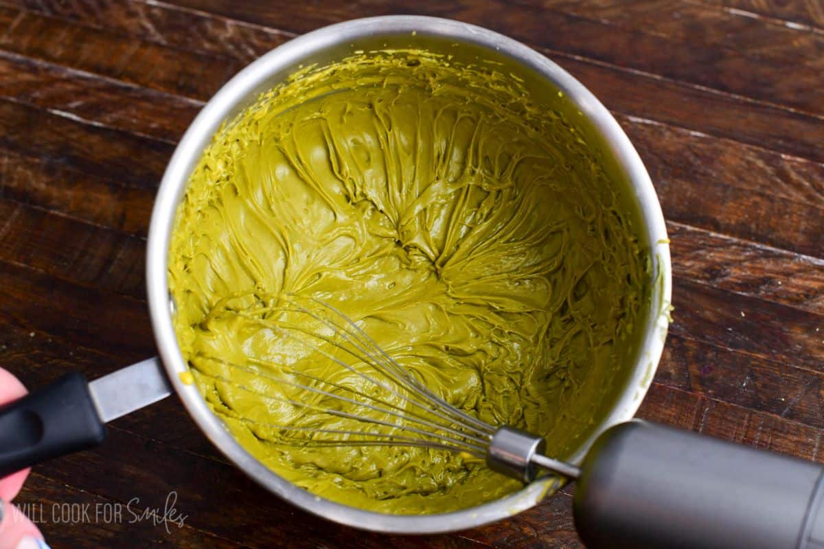 Pistachio paste whisked into egg yolk custard in a saucepan, creating a thick green pistachio cream mixture.