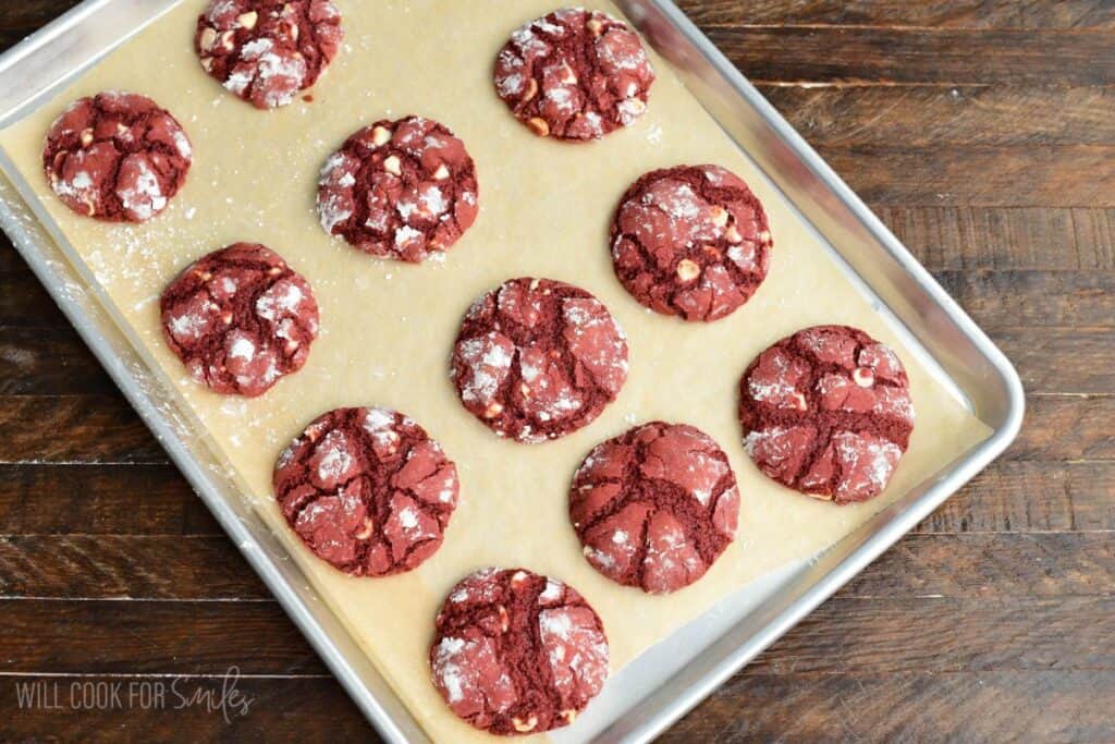 Freshly baked red velvet cream cheese cookies with powdered sugar tops on a baking sheet.