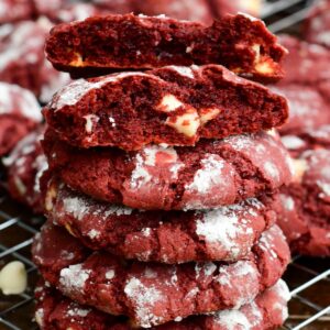 Stack of red velvet cream cheese cookies with one broken open, showing the soft center and white chocolate chips.