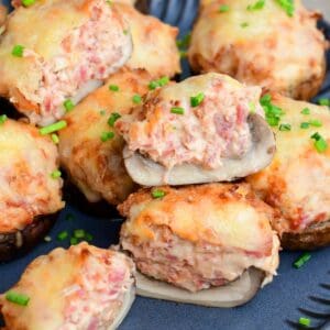 Close-up of Reuben stuffed mushrooms with melted Swiss cheese and chopped chives, one mushroom cut open to show the creamy corned beef filling.