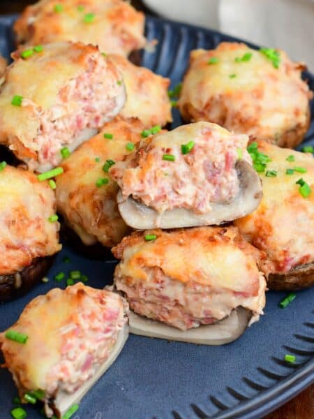 Close-up of Reuben stuffed mushrooms with melted Swiss cheese and chopped chives, one mushroom cut open to show the creamy corned beef filling.