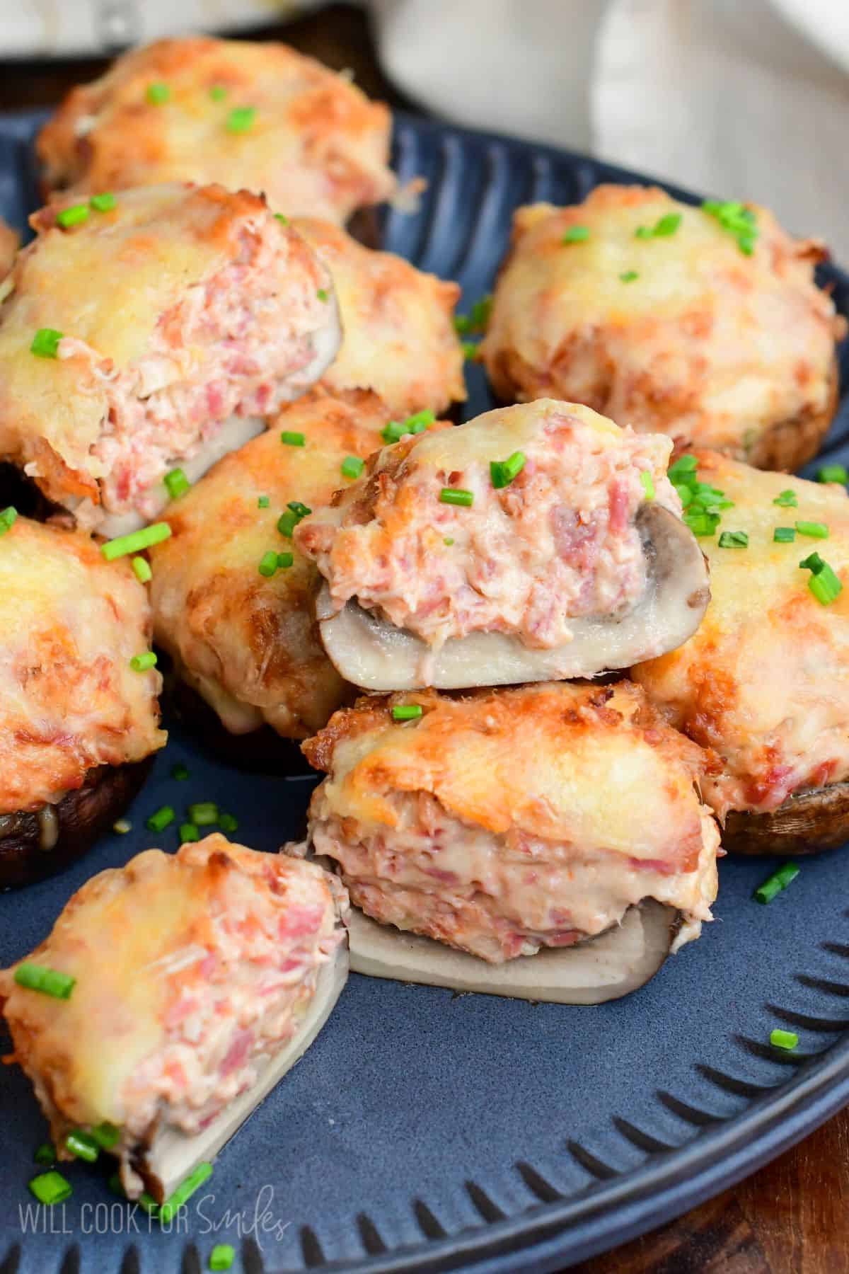 Close-up of Reuben stuffed mushrooms with melted Swiss cheese and chopped chives, one mushroom cut open to show the creamy corned beef filling.