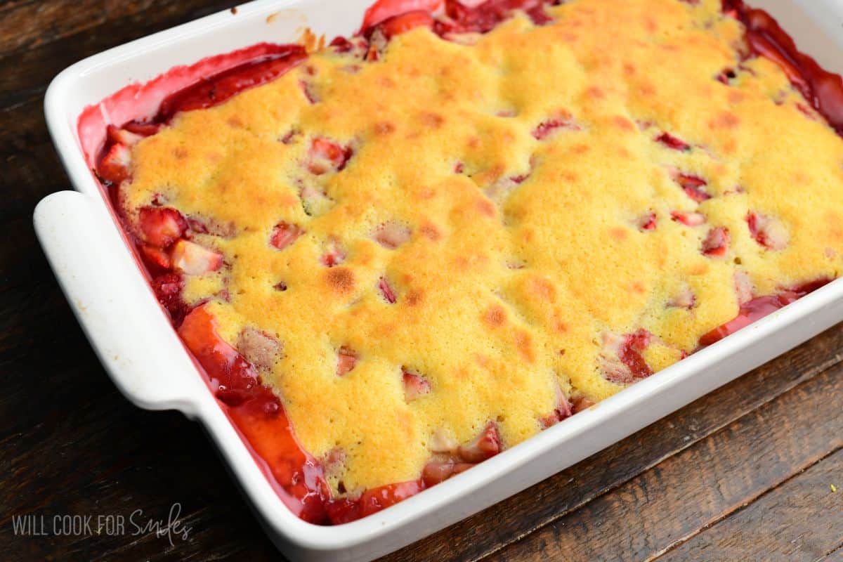 Close-up of baked strawberry basil cobbler with golden cake topping and bubbling strawberry filling around the edges.