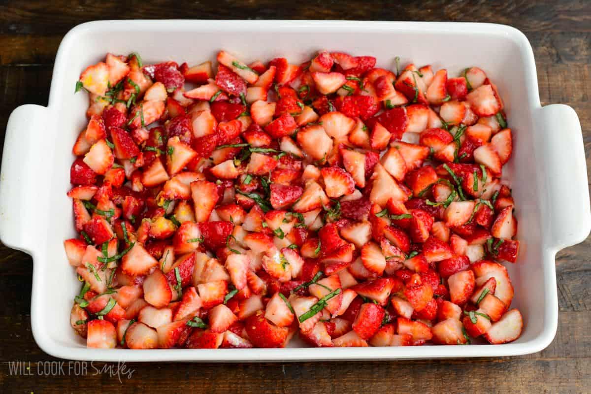 Baking dish filled with chopped strawberries mixed with sugar and fresh basil, spread evenly for cobbler.