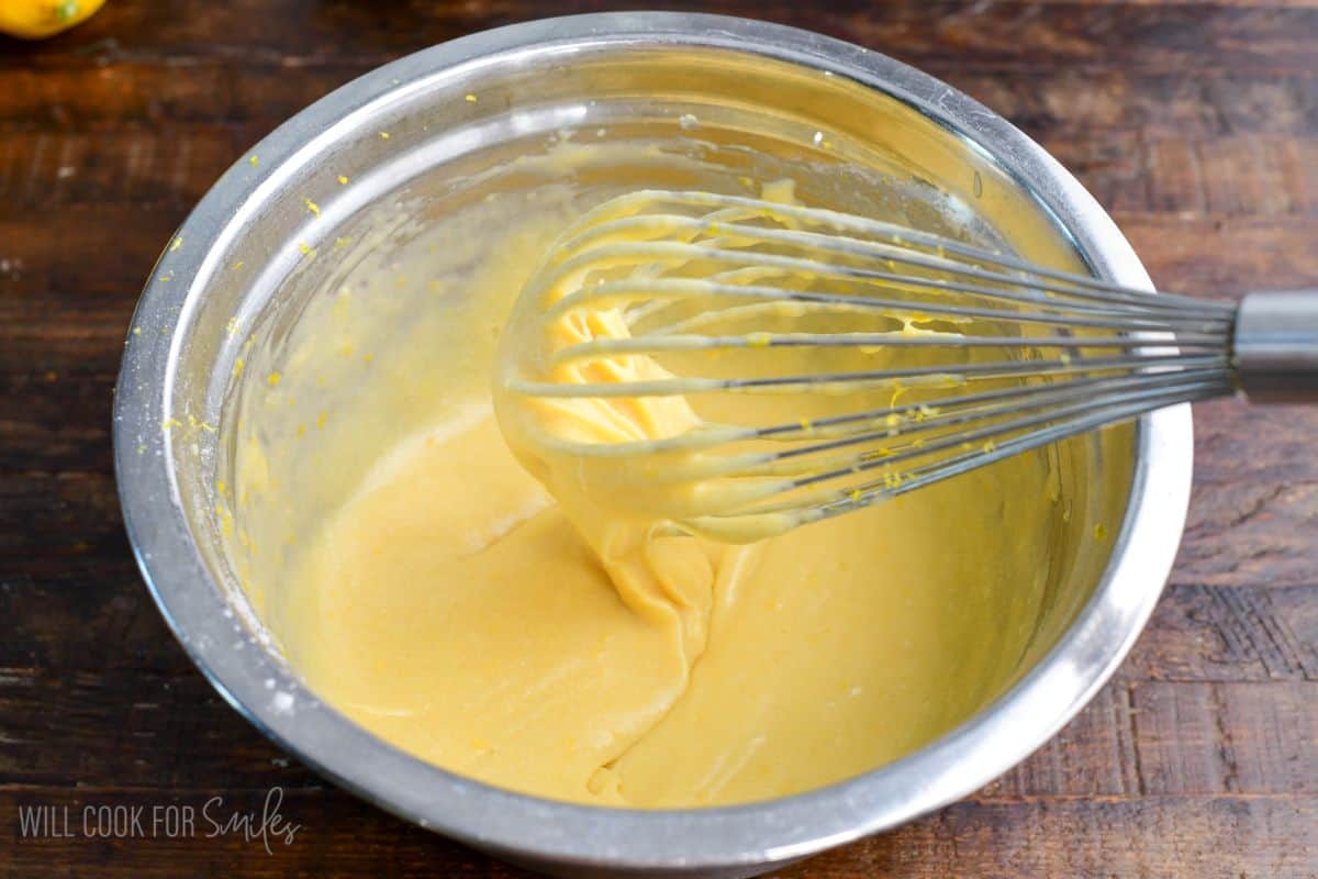 Metal mixing bowl with smooth yellow batter being whisked until creamy and lump-free.