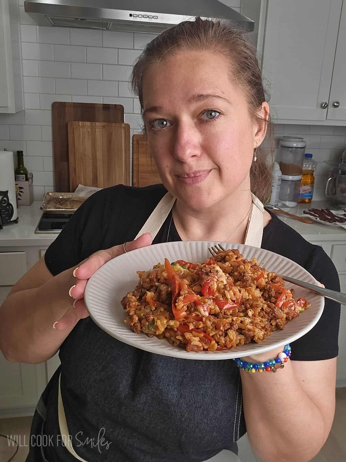 Person holding a plate of beef enchilada rice casserole in a home kitchen.