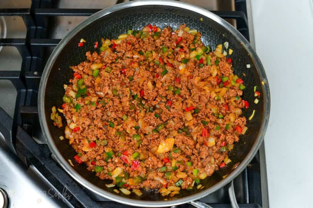Cooked chorizo crumbles mixed with sautéed onions, green peppers, and red chilies in a skillet on the stovetop.