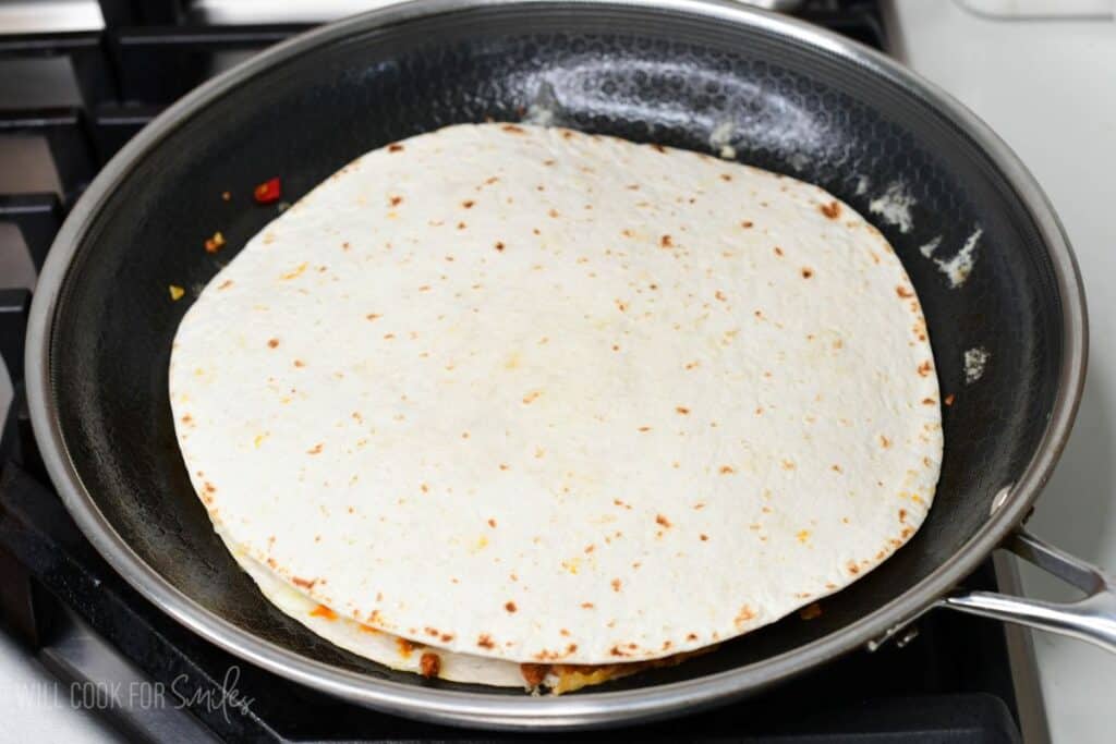 Quesadilla cooking in a skillet with a tortilla folded over the filling on the stovetop.