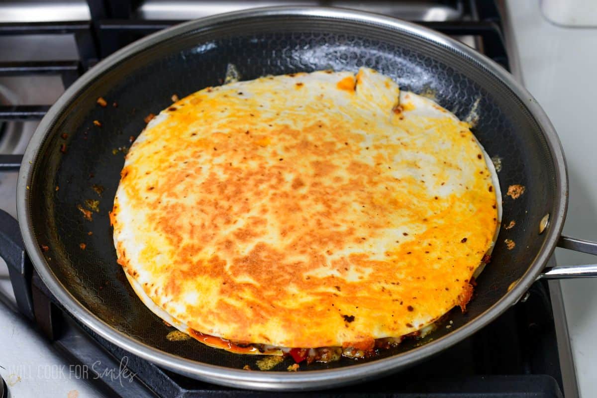 Quesadilla cooking in a skillet, flipped and browned on the outside with melted cheese inside.