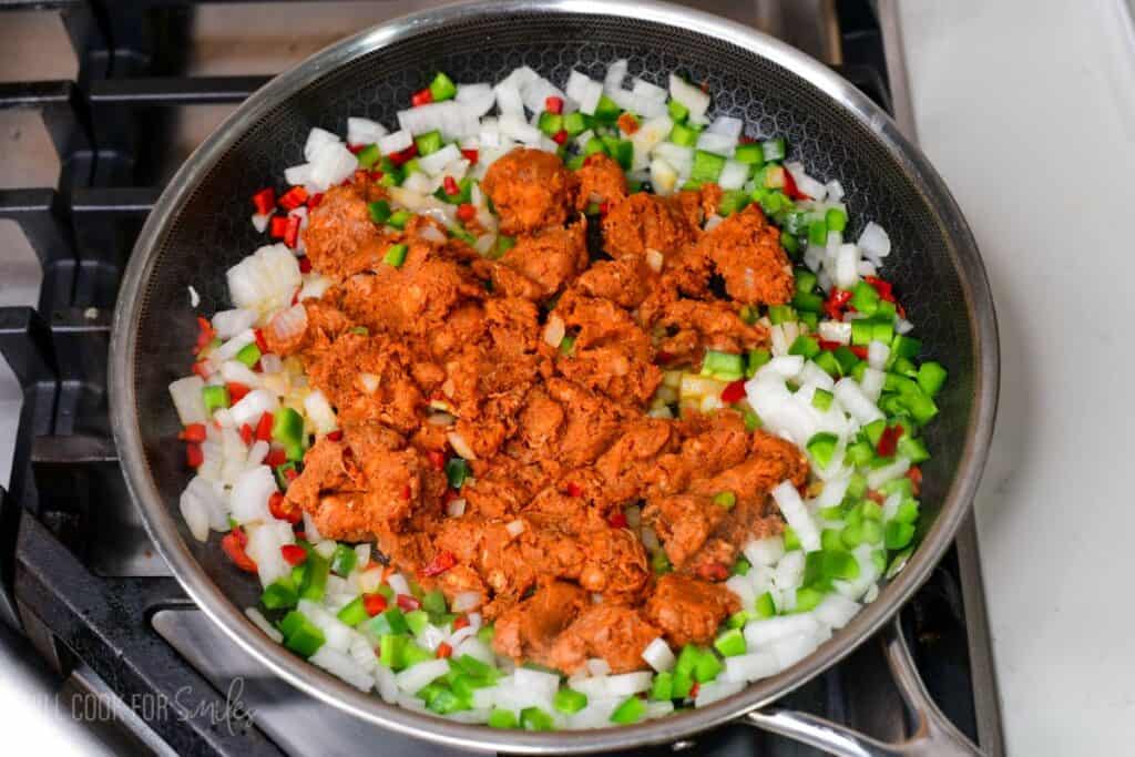 Chorizo cooking in a skillet with diced onions, green peppers, and red chilies on the stovetop.