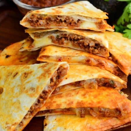 Stacked chorizo quesadilla wedges with melted cheese and savory filling, served with salsa on a wooden board.