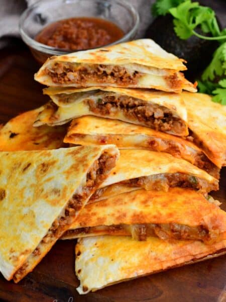 Stacked chorizo quesadilla wedges with melted cheese and savory filling, served with salsa on a wooden board.