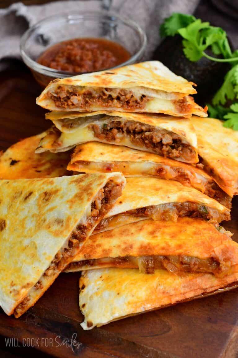 Stacked chorizo quesadilla wedges with melted cheese and savory filling, served with salsa on a wooden board.