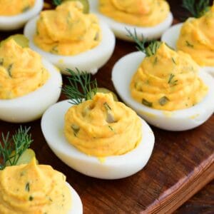 Dill pickle deviled eggs arranged on a wooden serving board, garnished with pickle slices and fresh dill.