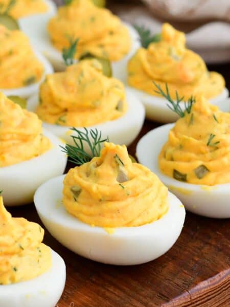 Close-up of dill pickle deviled eggs with creamy filling, garnished with fresh dill and pickle slices on a wooden board.