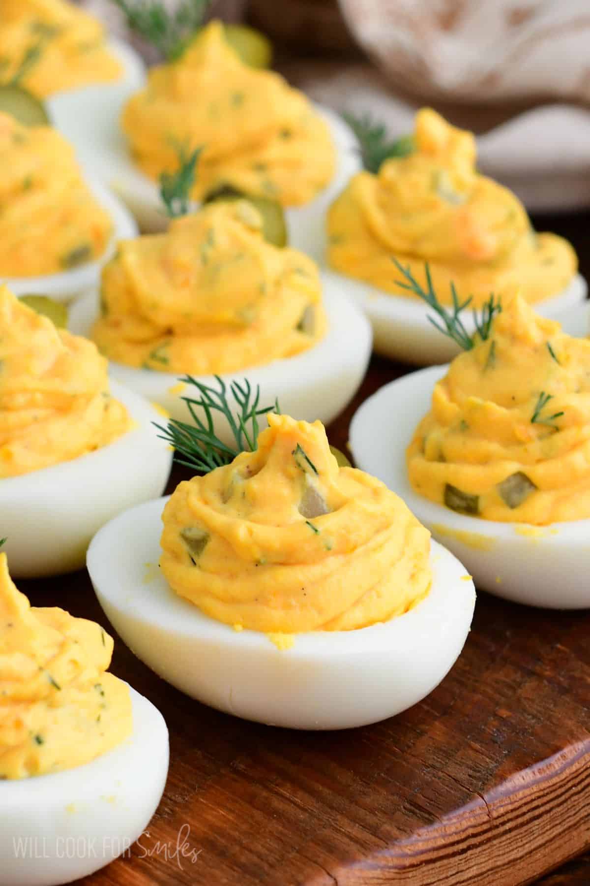 Close-up of dill pickle deviled eggs with creamy filling, garnished with fresh dill and pickle slices on a wooden board.