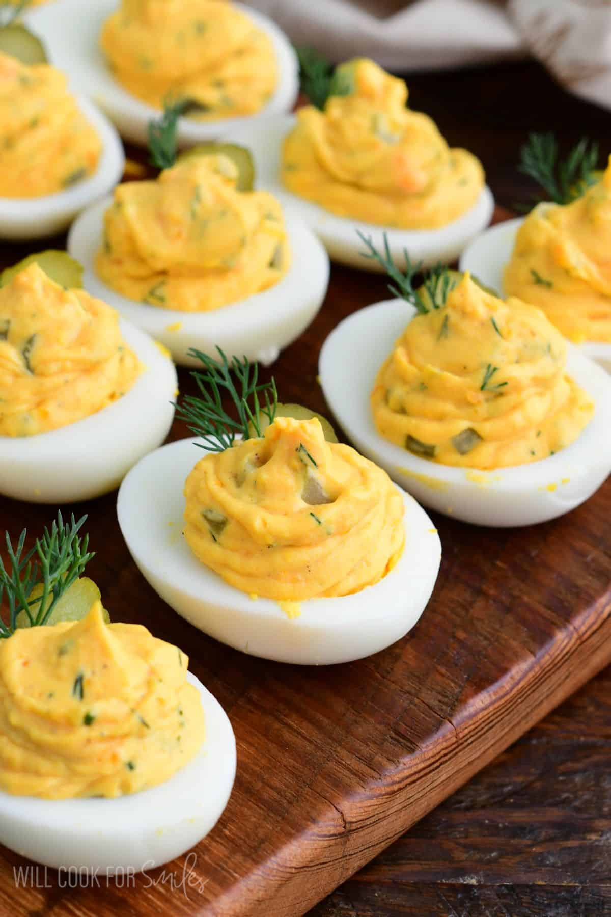 Dill pickle deviled eggs arranged on a wooden serving board, garnished with pickle slices and fresh dill.