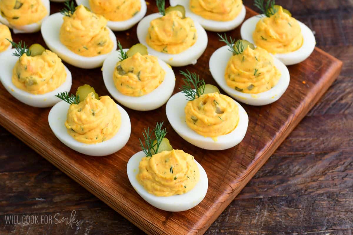 Close-up of dill pickle deviled eggs with creamy filling, topped with pickle slices and fresh dill on a wooden board.