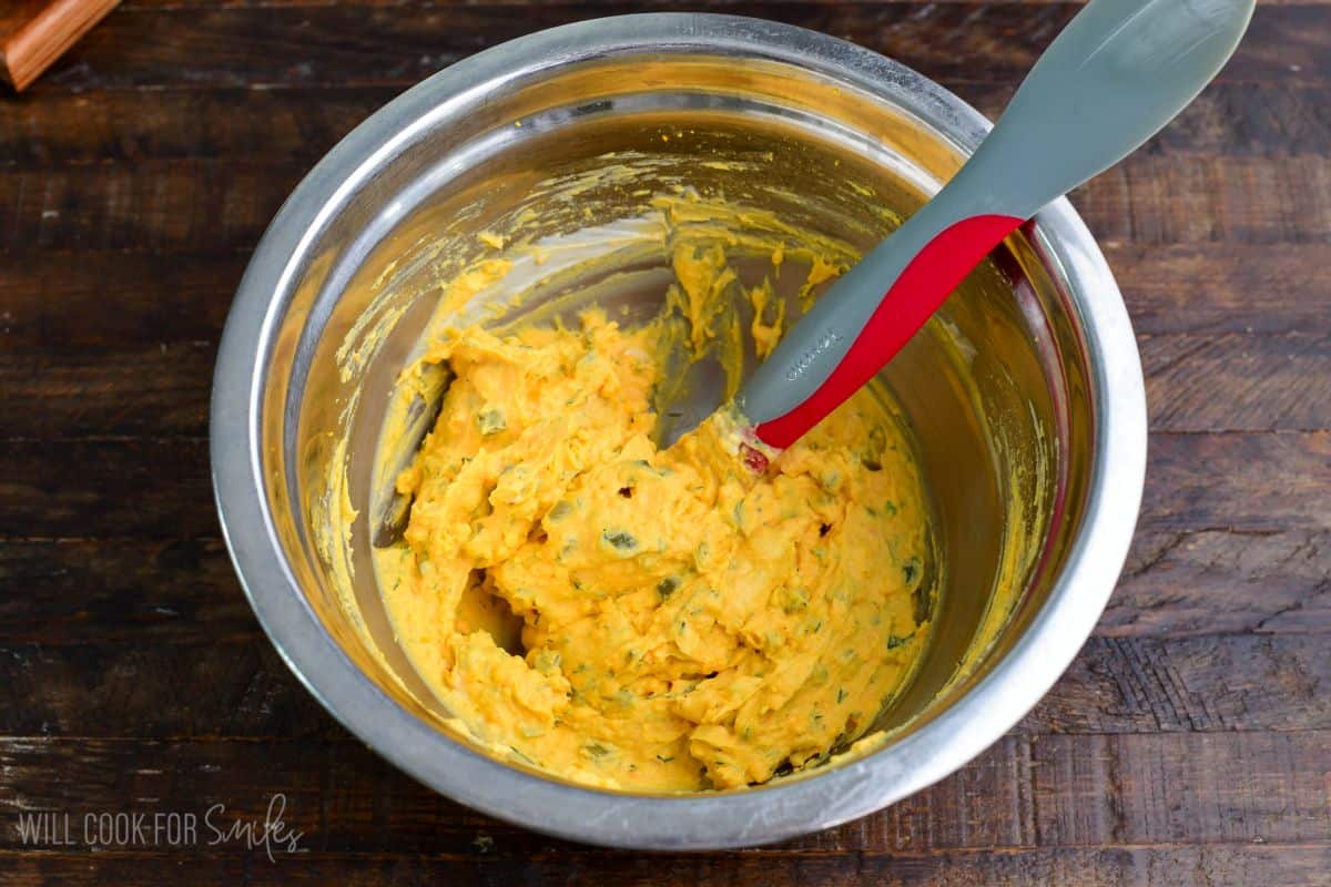 Creamy deviled egg filling being mixed in a metal bowl, with visible bits of dill and chopped pickles.